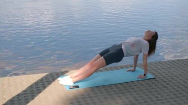 Genç bir kız yoga yapıyor. Akşamları nehrin kıyısında yoga minderinde.