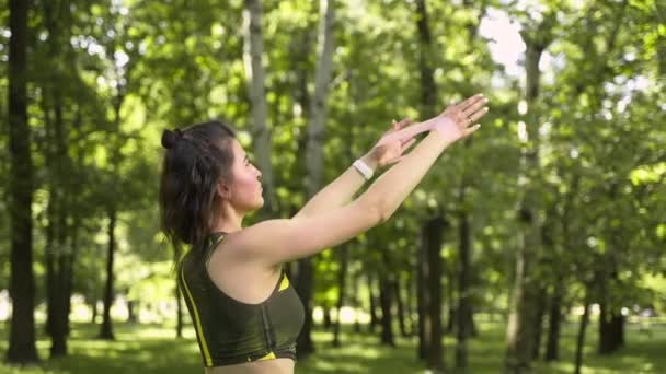 公園や森の中でフィットネス用の伸縮性のあるスポーツをする少女です ヨガマットに緑のスーツを着て — ストック動画