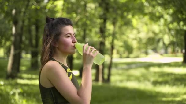 公園や森の中で水を飲む少女 緑のトラックスーツを着て — ストック動画