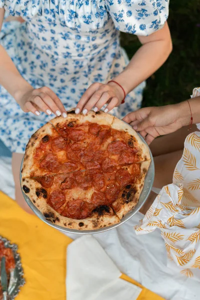 two girls take pizza at a picnic in the park in nature. blue dress, yellow dress. big frame