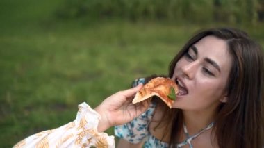 Sarı elbiseli bir kız tatilde parkta mavi elbiseli bir kıza pizza veriyor. Sarı elbise, mavi elbise