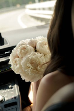 Gelin elinde çiçeklerle arabaya biniyor.
