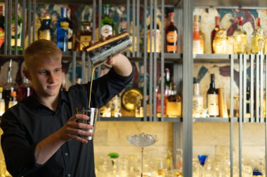 Barmen bir barda kokteyl hazırlıyor. Alkol ve şurup döker. Buz kullanır ve buzu kırar.