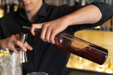 Barmen bir barda kokteyl hazırlıyor. Alkol ve şurup döker. Buz kullanır ve buzu kırar.