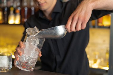 Barmen bir barda kokteyl hazırlıyor. Alkol ve şurup döker. Buz kullanır ve buzu kırar.