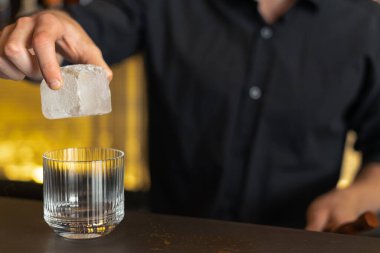 Barmen bir barda kokteyl hazırlıyor. Alkol ve şurup döker. Buz kullanır ve buzu kırar.