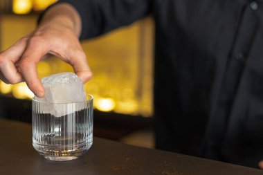 Barmen bir barda kokteyl hazırlıyor. Alkol ve şurup döker. Buz kullanır ve buzu kırar.