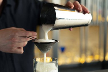 Barmen bir barda kokteyl hazırlıyor. Alkol ve şurup döker. Buz kullanır ve buzu kırar.