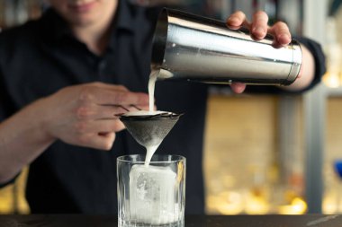 Barmen bir barda kokteyl hazırlıyor. Alkol ve şurup döker. Buz kullanır ve buzu kırar.