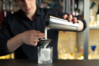 Barmen bir barda kokteyl hazırlıyor. Alkol ve şurup döker. Buz kullanır ve buzu kırar.