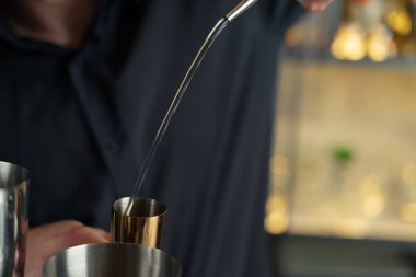 Barmen bir barda kokteyl hazırlıyor. Alkol ve şurup döker. Buz kullanır ve buzu kırar.