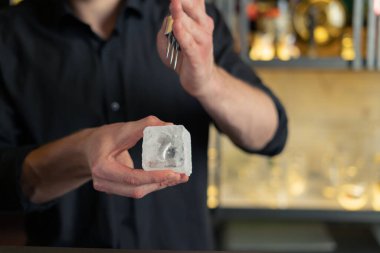 Barmen bir barda kokteyl hazırlıyor. Alkol ve şurup döker. Buz kullanır ve buzu kırar.