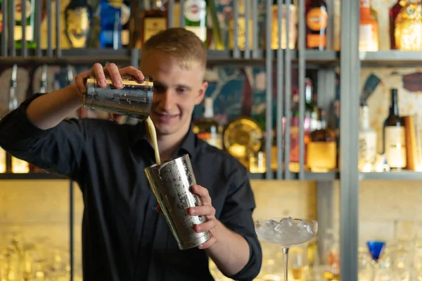 Barmen bir barda kokteyl hazırlıyor. Alkol ve şurup döker. Buz kullanır ve buzu kırar.