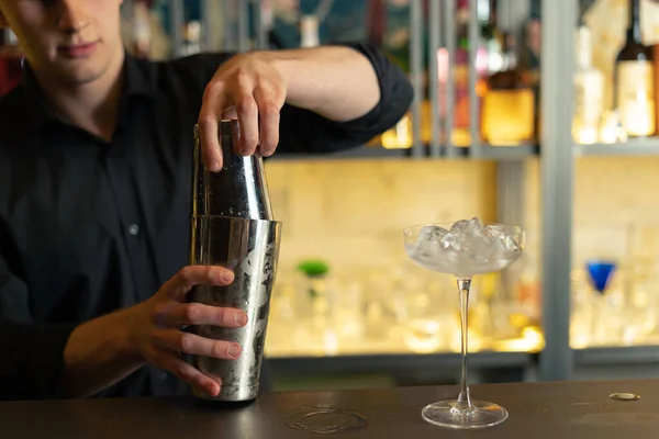 Barmen bir barda kokteyl hazırlıyor. Alkol ve şurup döker. Buz kullanır ve buzu kırar.