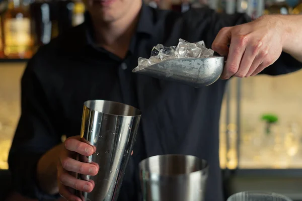 Barmen bir barda kokteyl hazırlıyor. Alkol ve şurup döker. Buz kullanır ve buzu kırar.
