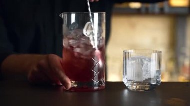 Barmen bir barda kokteyl hazırlıyor. Alkol ve şurup döker. Buz kullanır ve buzu kırar.
