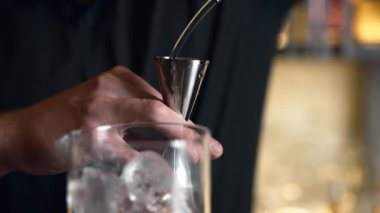 Barmen bir barda kokteyl hazırlıyor. Alkol ve şurup döker. Buz kullanır ve buzu kırar.
