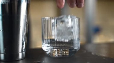Barmen bir barda kokteyl hazırlıyor. Alkol ve şurup döker. Buz kullanır ve buzu kırar.