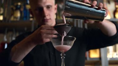 Barmen bir barda kokteyl hazırlıyor. Alkol ve şurup döker. Buz kullanır ve buzu kırar.