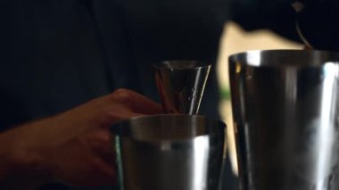 Barmen bir barda kokteyl hazırlıyor. Alkol ve şurup döker. Buz kullanır ve buzu kırar.