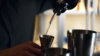 Barmen bir barda kokteyl hazırlıyor. Alkol ve şurup döker. Buz kullanır ve buzu kırar.