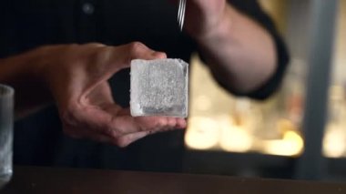 Barmen bir barda kokteyl hazırlıyor. Alkol ve şurup döker. Buz kullanır ve buzu kırar.