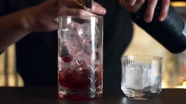 Barmen bir barda kokteyl hazırlıyor. Alkol ve şurup döker. Buz kullanır ve buzu kırar.