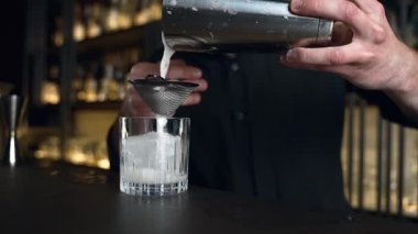 Barmen bir barda kokteyl hazırlıyor. Alkol ve şurup döker. Buz kullanır ve buzu kırar.