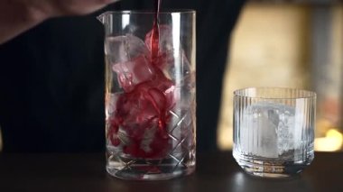 Barmen bir barda kokteyl hazırlıyor. Alkol ve şurup döker. Buz kullanır ve buzu kırar.