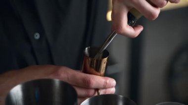 Barmen bir barda kokteyl hazırlıyor. Alkol ve şurup döker. Buz kullanır ve buzu kırar.