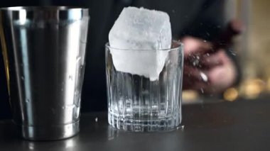 Barmen bir barda kokteyl hazırlıyor. Alkol ve şurup döker. Buz kullanır ve buzu kırar.