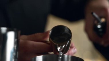 Barmen bir barda kokteyl hazırlıyor. Alkol ve şurup döker. Buz kullanır ve buzu kırar.