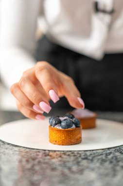 Genç aşçı kız tatlı yapıyor. Tatlı ve kek pişirir. Boşlukları doldurur ve meyveleri hazırlar. Pişirme, tatlı, tatlılar, karmaşık pişirme süreçleri.