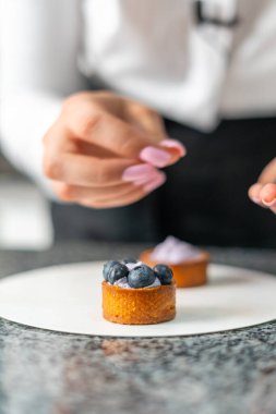 Genç aşçı kız tatlı yapıyor. Tatlı ve kek pişirir. Boşlukları doldurur ve meyveleri hazırlar. Pişirme, tatlı, tatlılar, karmaşık pişirme süreçleri.