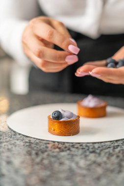 Genç aşçı kız tatlı yapıyor. Tatlı ve kek pişirir. Boşlukları doldurur ve meyveleri hazırlar. Pişirme, tatlı, tatlılar, karmaşık pişirme süreçleri.