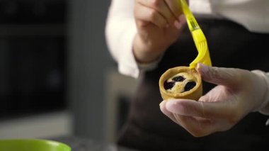 Genç aşçı kız tatlı yapıyor. Tatlı ve kek pişirir. Boşlukları doldurur ve meyveleri hazırlar. Pişirme, tatlı, tatlılar, karmaşık pişirme süreçleri.