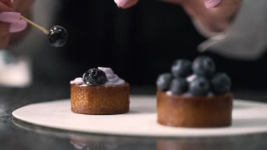 Genç aşçı kız tatlı yapıyor. Tatlı ve kek pişirir. Boşlukları doldurur ve meyveleri hazırlar. Pişirme, tatlı, tatlılar, karmaşık pişirme süreçleri.