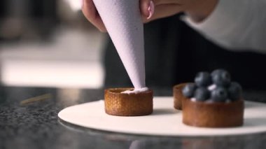 Genç aşçı kız tatlı yapıyor. Tatlı ve kek pişirir. Boşlukları doldurur ve meyveleri hazırlar. Pişirme, tatlı, tatlılar, karmaşık pişirme süreçleri.