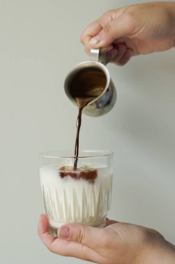 girl pours coffee into milk in a glass on a white background