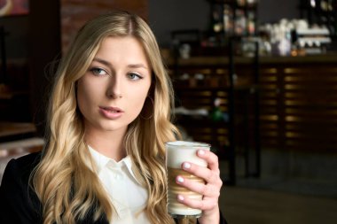 White blonde woman holding a glass of coffee in her hand. Portrait of a beautiful smiling girl. Indoor cafe. Morning summer mood. High quality photo