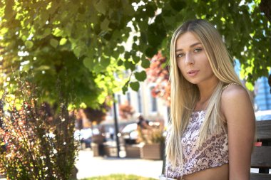 Çekici, neşeli, düz saçlı kızın portresi güzel havanın tadını çıkarıyor şehir merkezinin dışında bankta otururken eğleniyor. Yüksek kalite fotoğraf