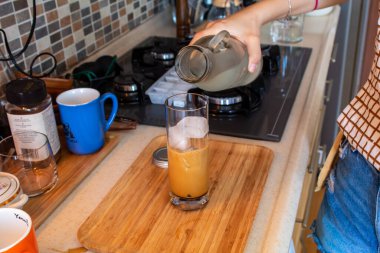 A woman hand preparing a glass of cold coffee on a wooden cutting board at kitchen. High quality photo