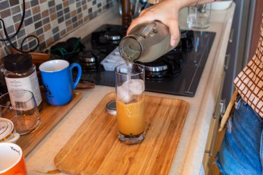 A woman hand preparing a glass of cold coffee on a wooden cutting board at kitchen. High quality photo