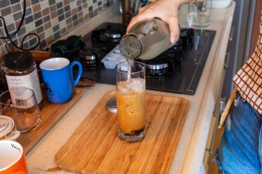 A woman hand preparing a glass of cold coffee on a wooden cutting board at kitchen. High quality photo