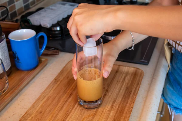 A woman hand preparing a glass of cold coffee on a wooden cutting board at kitchen. High quality photo