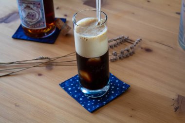 A long glass of black foamy coffee with a glasss coffee bottle on a wooden table. Concept. High quality photo