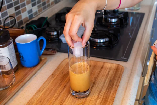 A woman hand preparing a glass of cold coffee on a wooden cutting board at kitchen. High quality photo