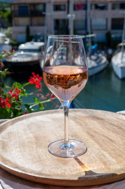 Fransız Riviera Cote d 'Azur' da yaz mevsimi, Cotes de Provence 'den soğuk gül şarabı içmek Port Grimaud, Var, Fransa' da güneşli açık teraslarda arka planda botlar ve yatlarla