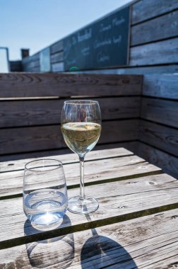 Güneşli bir günde deniz manzaralı terasta sunulan beyaz şarap ve maden suyu bardakları, yaz tatili.