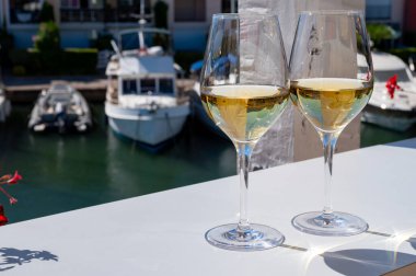 Fransız Riviera Cote d 'Azur' da yaz mevsiminde Cotes de Provence 'den gelen soğuk beyaz şarabı arka planda tekne ve yatlarla Port Grimaud, Var, Fransa' daki güneşli açık terasta içerken.